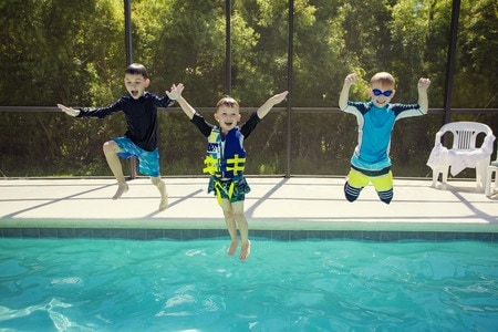 three boys jumping into a pool