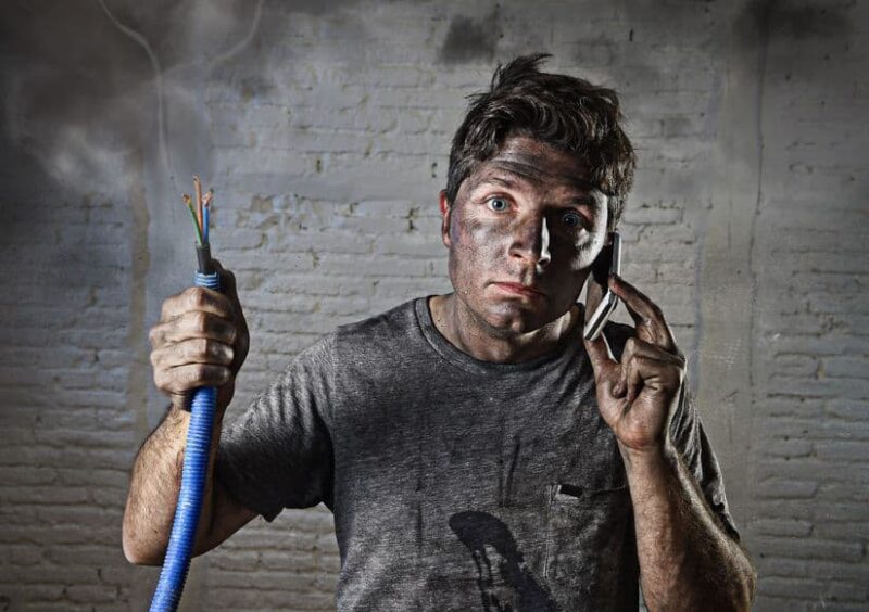 man covered in ash holding electrical cable